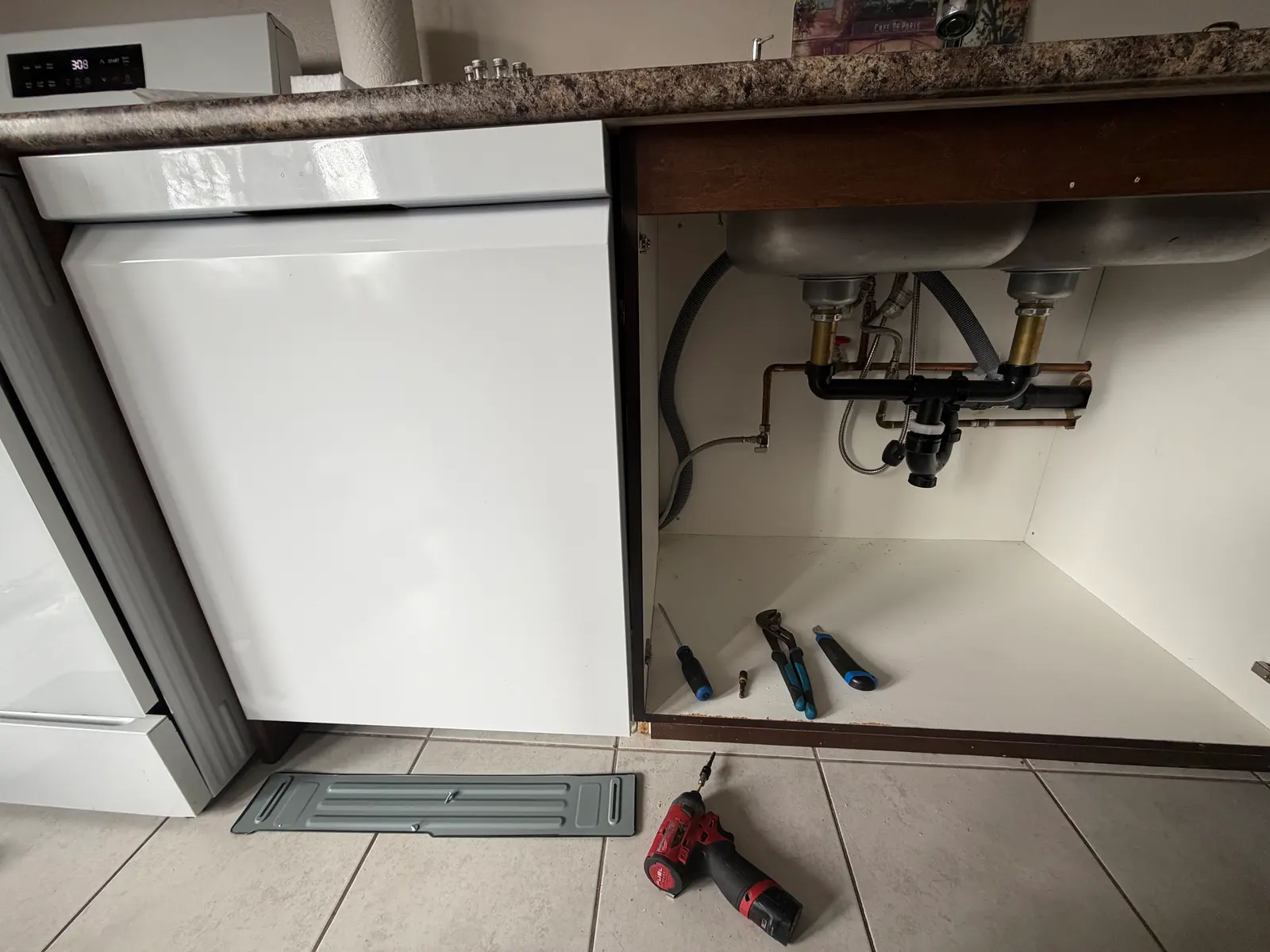 Dishwasher installed beside an open sink cabinet with water and drain connections during installation in Ottawa