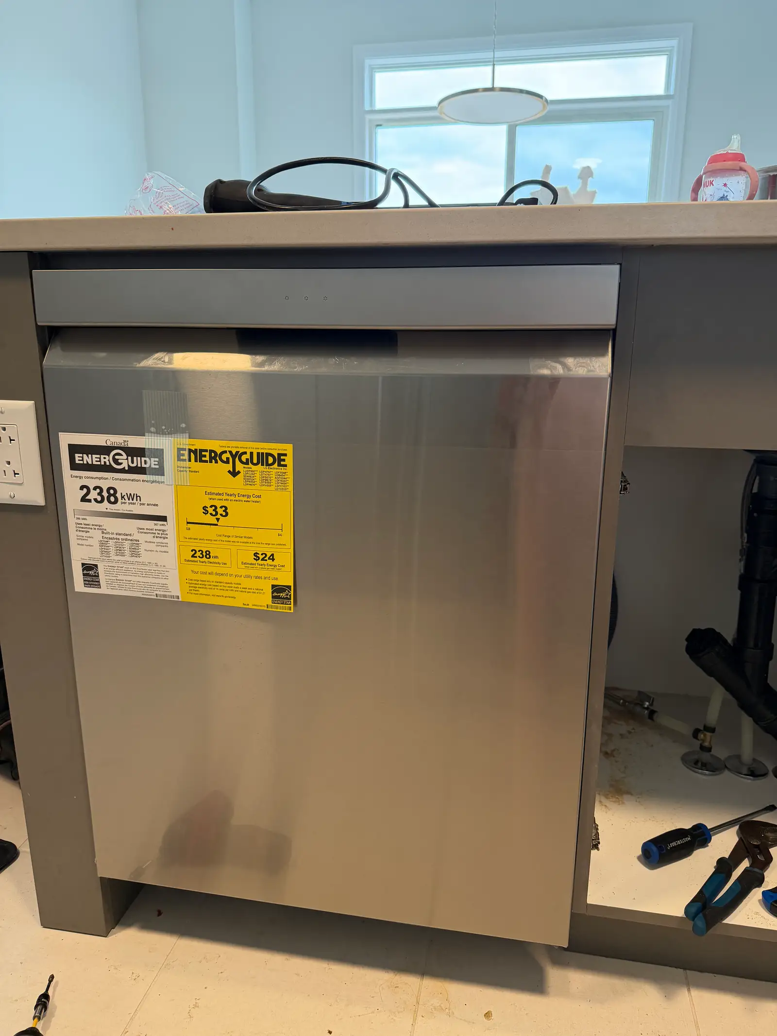 Newly installed stainless steel dishwasher with power cord and open sink plumbing cabinet in an Ottawa kitchen
